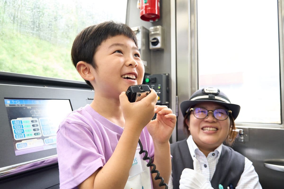 車掌さんの隣でアナウンス体験をする子ども